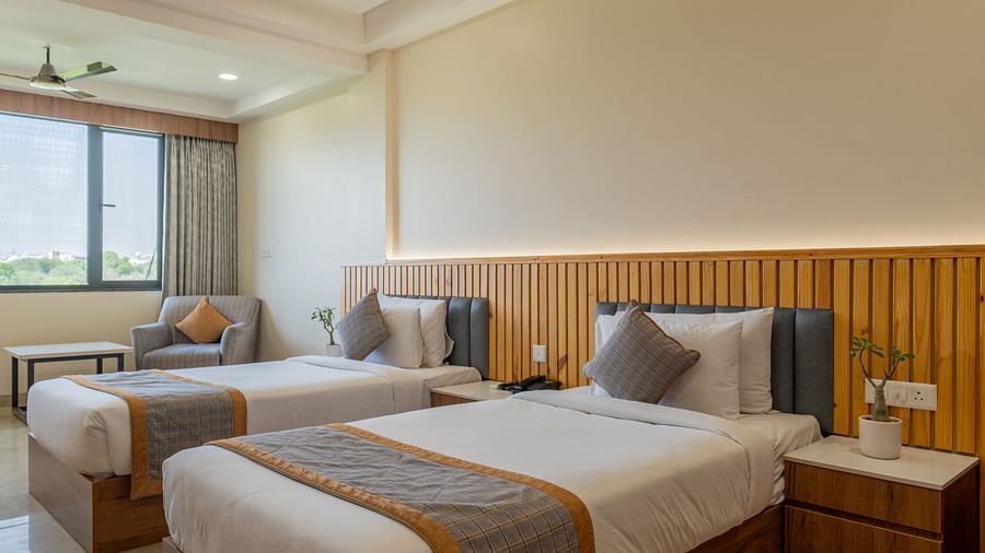 Twin bedroom at Hotel Highway King, Bagru, with bedside tables, large window, and upholstered headboards.