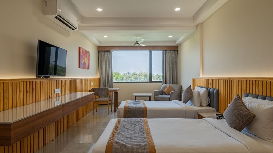 A bedroom at Hotel Highway King, Bagru, with desk, television, large window, ceiling fan, and bedside tables.