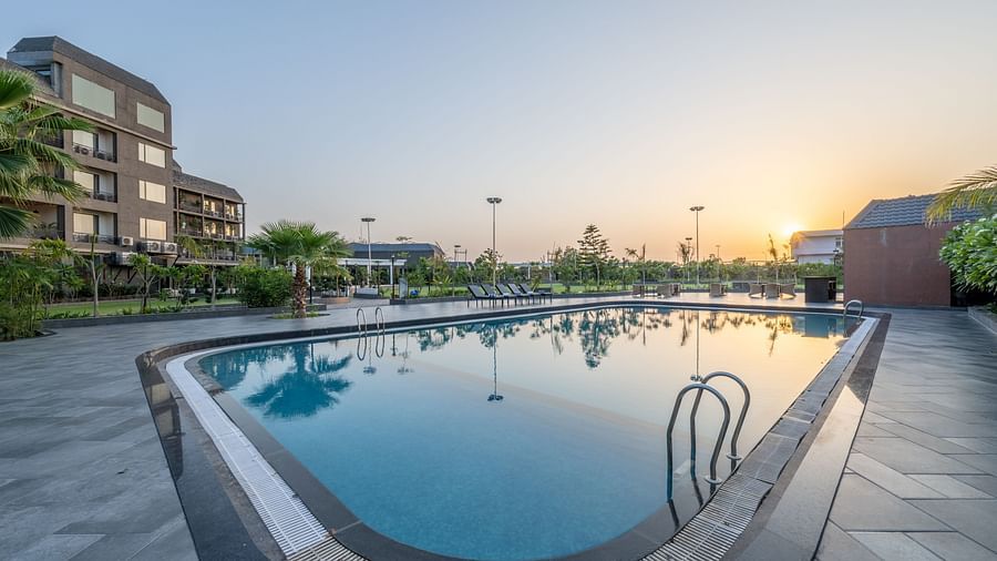 Swimming pool area at Hotel Highway King, Bagru, with loungers, landscaped garden, and hotel building.