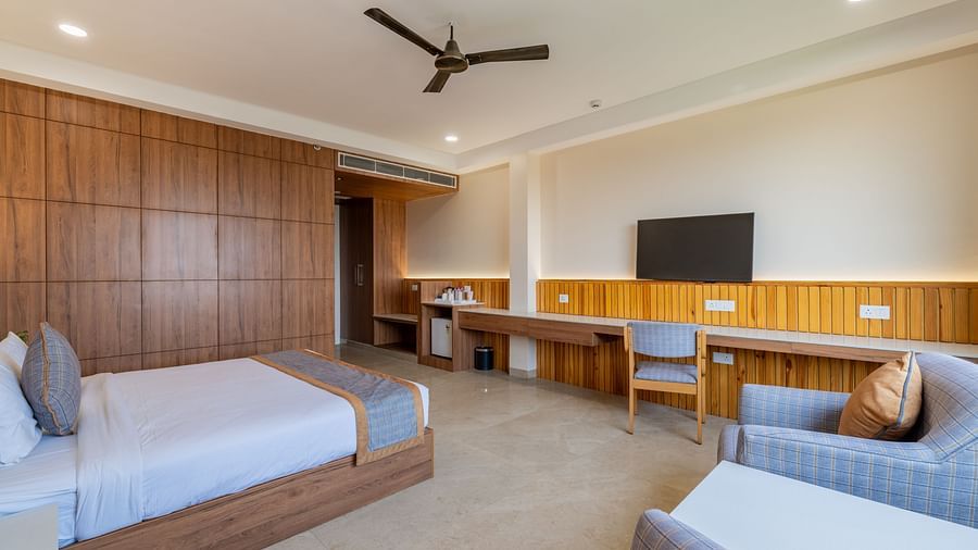 A back angle view of the club room at Hotel Highway King, Bagru, with a double bed, and arm chairs and an entertainment unit.