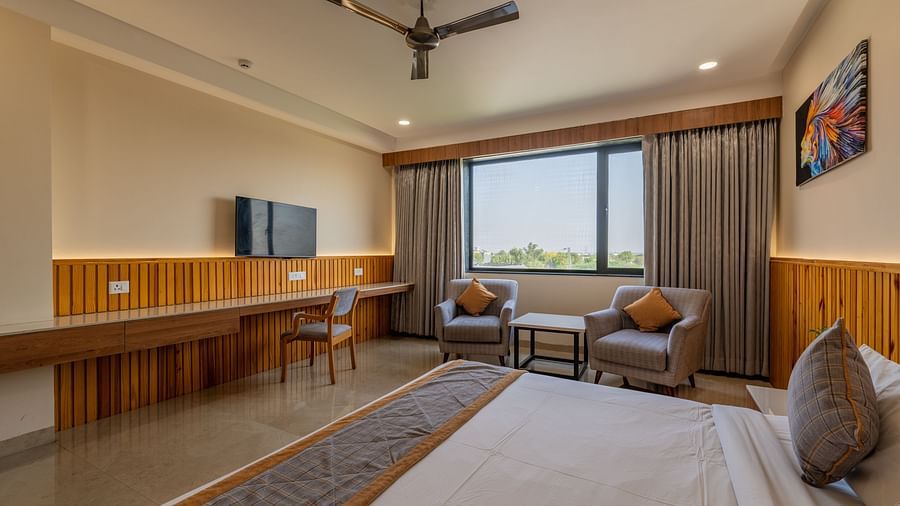 Club room at Hotel Highway King, Bagru, featuring a large bed with white linens, a wooden headboard, a ceiling fan, lounge chairs and a painting on the wall.