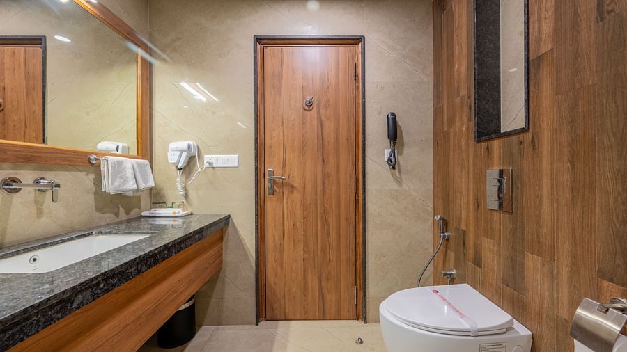 A wooden panelled washroom in Hotel Highway King, Bagru featuring a western commode, sink area and a large mirror.
