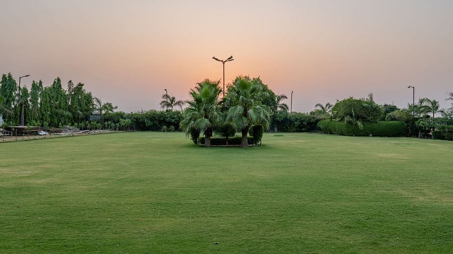 An extended view of the expansive open garden area in the premises of Hotel Highway King, Behror, seen with trees, and grass.