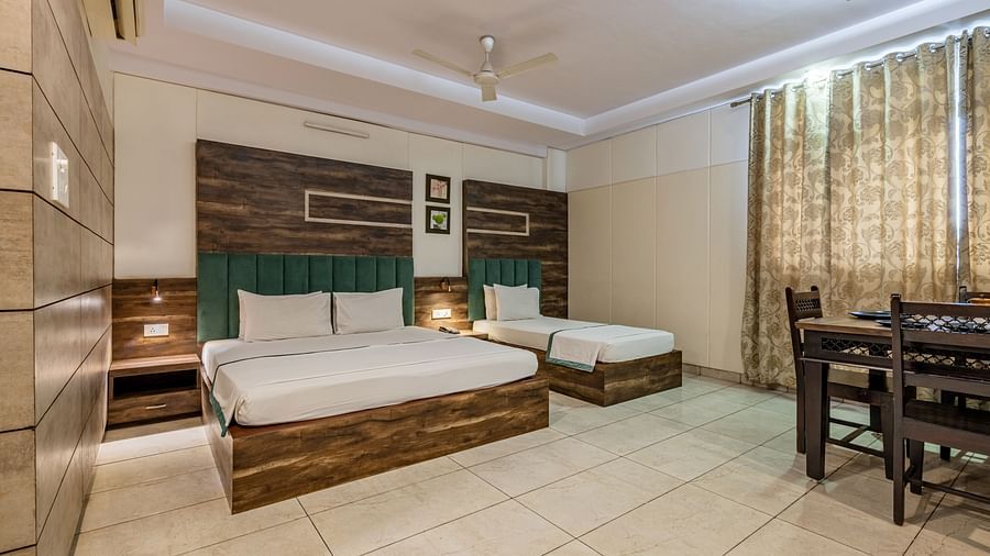 Extended view of the double and single bed, dining table and drawn curtains in the Suite of Hotel Highway King in Behror.