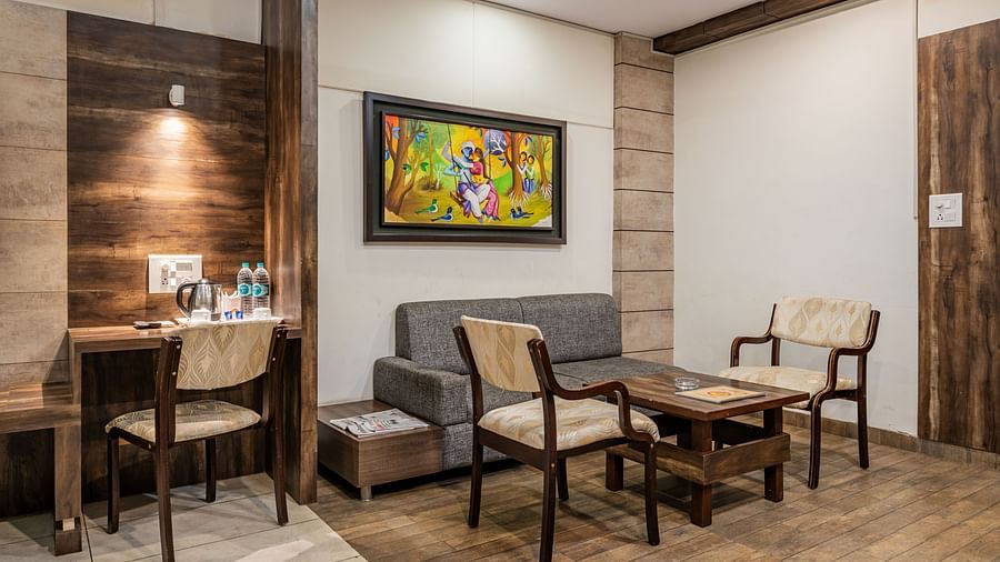 Separate living area furnished with an upholstered sofa, seating chairs for two, a center table and a word desk with dedicated lighting in the Suite of Hotel Highway King in Behror.