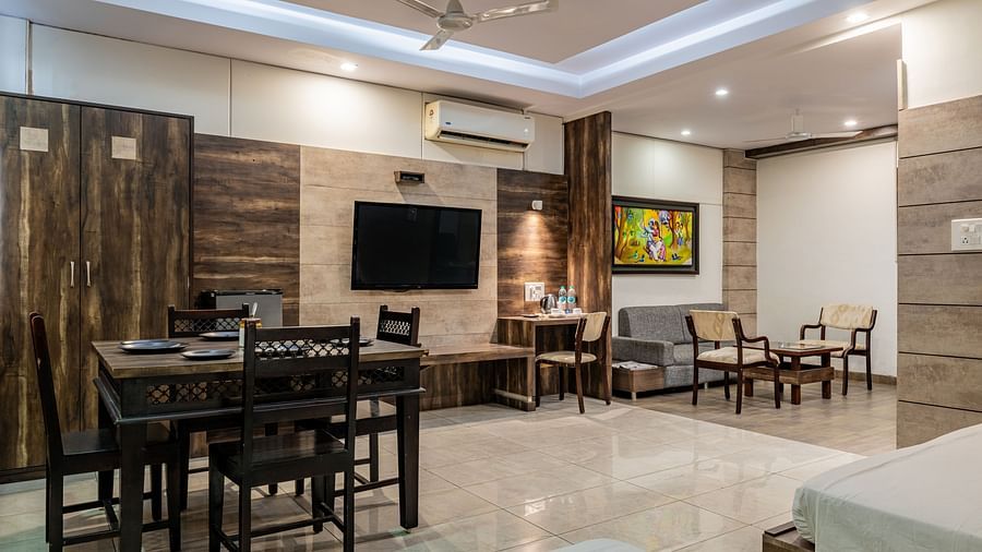 Dining table, wall-mounted TV, separate living area, and work desk in the Suite of Hotel Highway King in Behror.
