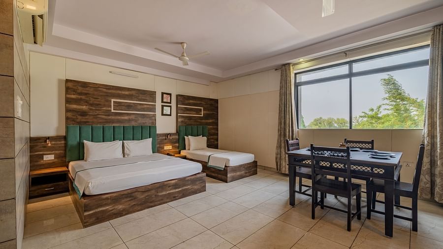 Extended view of the double and single bed, dining table and open glass windows in the Suite of Hotel Highway King in Behror.
