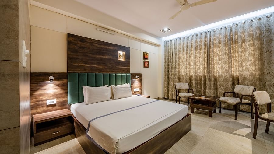 This spacious Maharaja Deluxe Room in Hotel Highway King, Behror, is furnished with a plush king size bed with upholstered headboard, ample lighting in the room, a seating area for two and curtains drawn together.