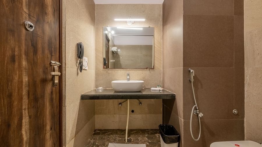 The bathroom of the Maharaja Deluxe Room in Hotel Highway King, Behror, is furnished with a western commode, a mirror, a sink and other necessary bathroom fittings.