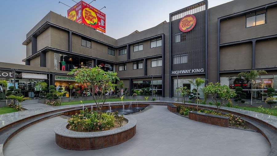 Facade and well-manicured lawn of Hotel Highway King, Behror, which also features a large logo of the property.