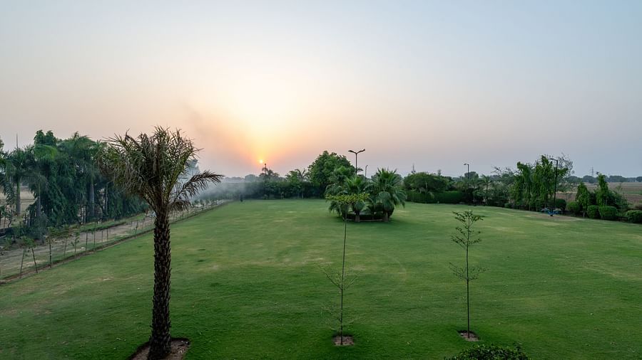 An extended view of the expansive open garden area in the premises of Hotel Highway King, Behror, seen with trees, and grass.