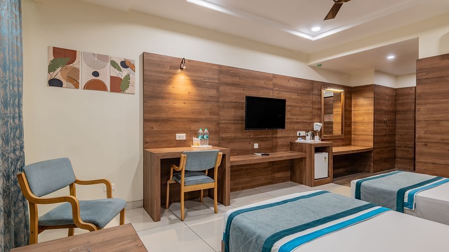 Warmly lit KIng Twin Bed Room with flat-screen TV, chairs, ceiling fan, and writing desk at Hotel Highway King, Bilaspur.