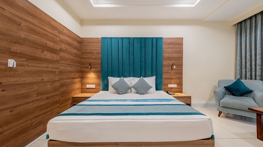 King size bed room with clean lines, minimalist design, and a teal padded headboard  with a lounge area at Hotel Highway King, Bilaspur.