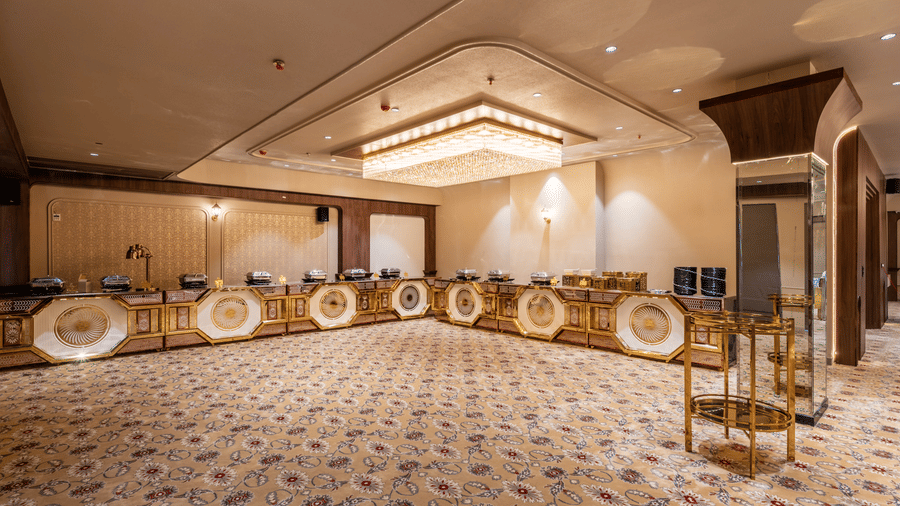 Banquet hall with round tables, covered chairs, decorative lighting, and patterned carpet.