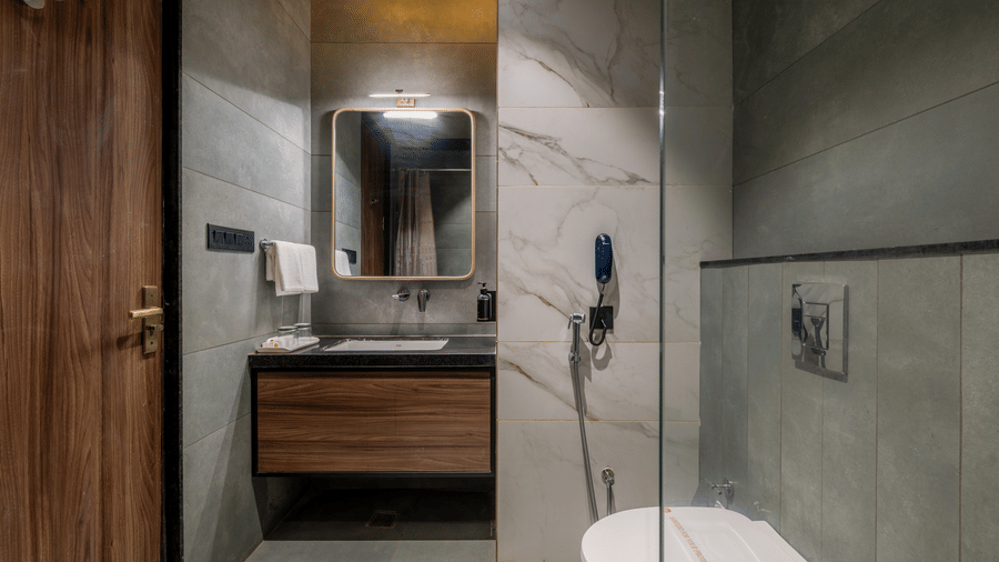 Bathroom with a washbasin, mirror, toilet, wooden vanity, and tiled walls.