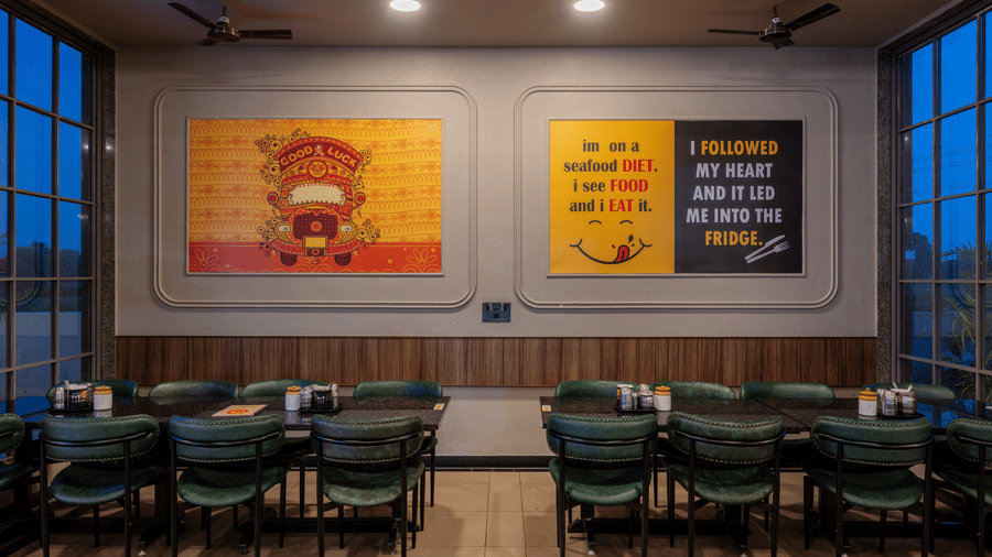Indoor restaurant seating area with framed wall art and cushioned dark green chairs.