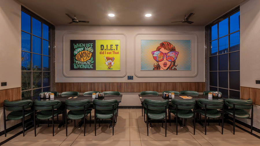 Indoor dining section with colorful framed wall posters and large window panels.