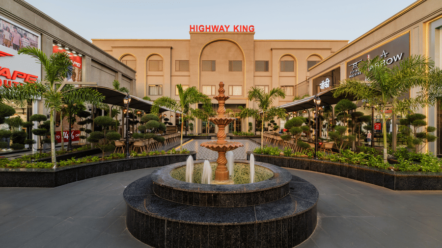 A central water fountain, surrounding storefronts, and a main building at Hotel Highway King, Harmada.