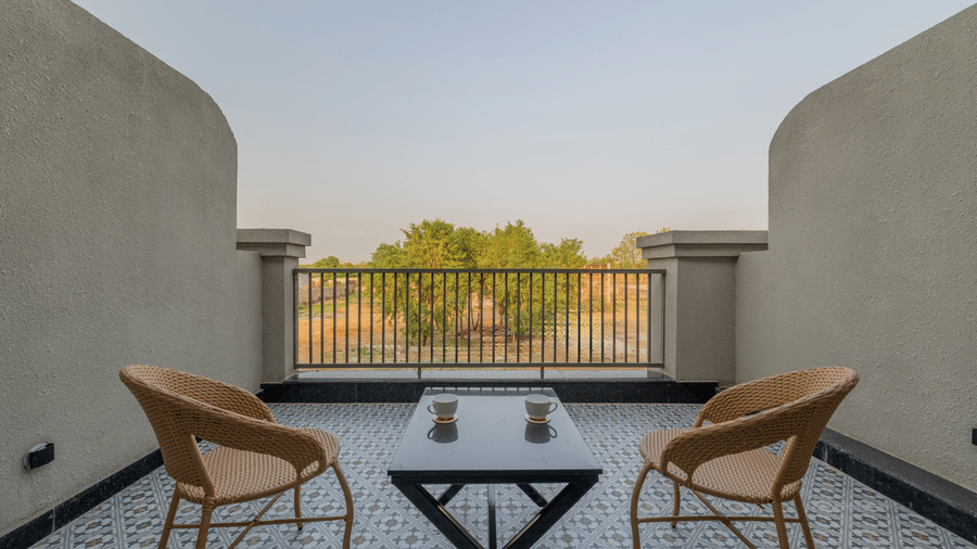 Open balcony space containing 2 chairs, a central coffee table, and a metal railing overlooking trees at Hotel Highway King, Harmada.