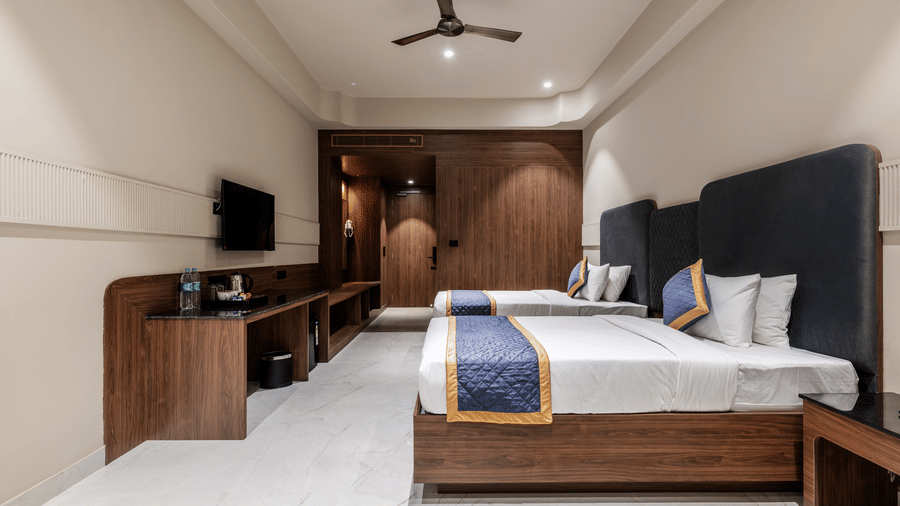 Inside a guestroom showcasing double beds, a wall television unit, and a ceiling fan in motion at Hotel Highway King, Harmada.