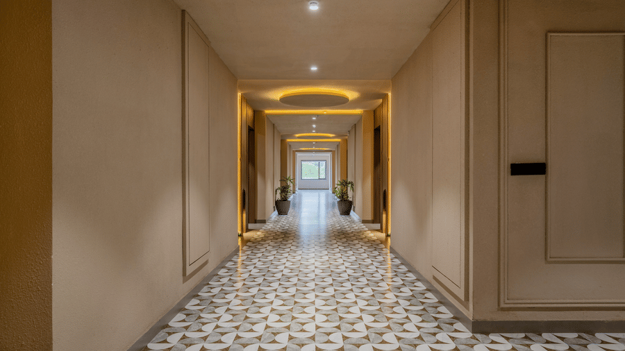 A straight hotel corridor with bright overhead lighting fixtures, smooth wall panels, and a repetitive geometric floor pattern at Hotel Highway King, Harmada.