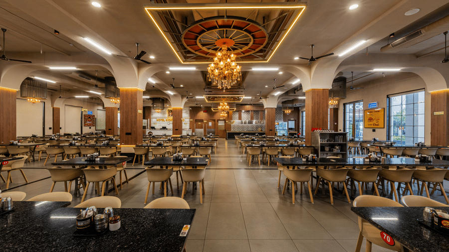 A restaurant interior featuring dining tables, chairs, and large decorative chandeliers at Hotel Highway King, Harmada.
