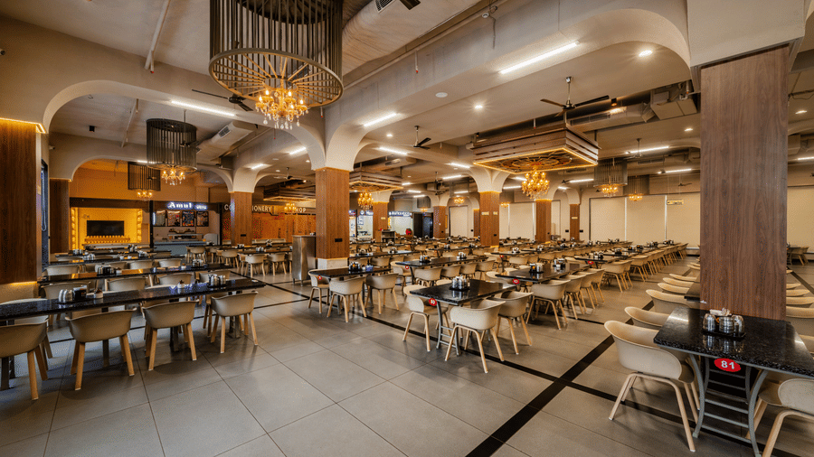 A large dining area showing rows of tables, dining chairs, and pendant light fixtures at Hotel Highway King, Harmada.