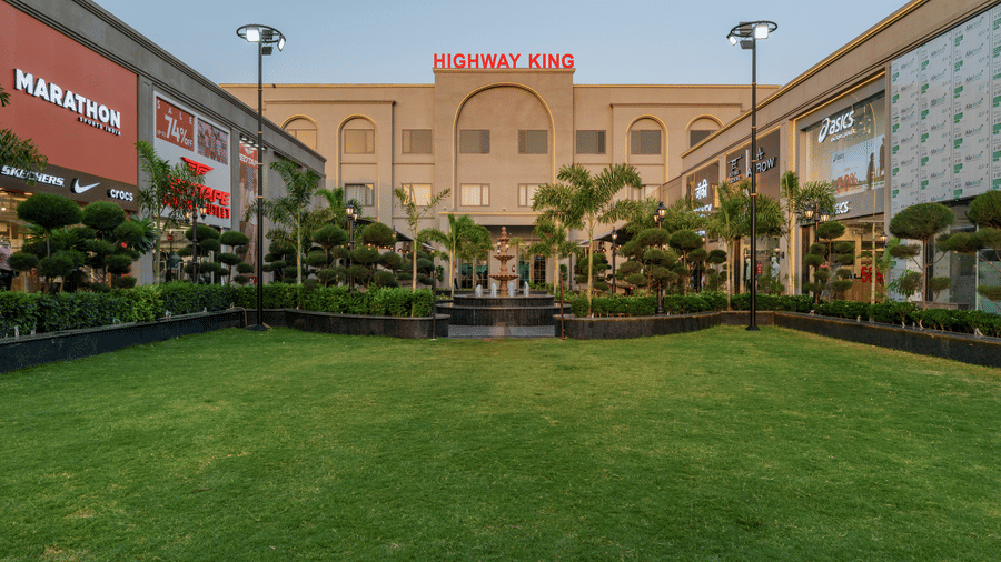 A wide green lawn with trimmed hedges, lampposts, and a large building at Hotel Highway King, Harmada.