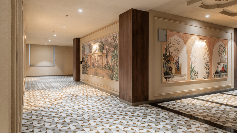 A wide hallway displaying detailed wall paintings, a wooden pillar, and patterned floor tiles at Hotel Highway King, Harmada.
