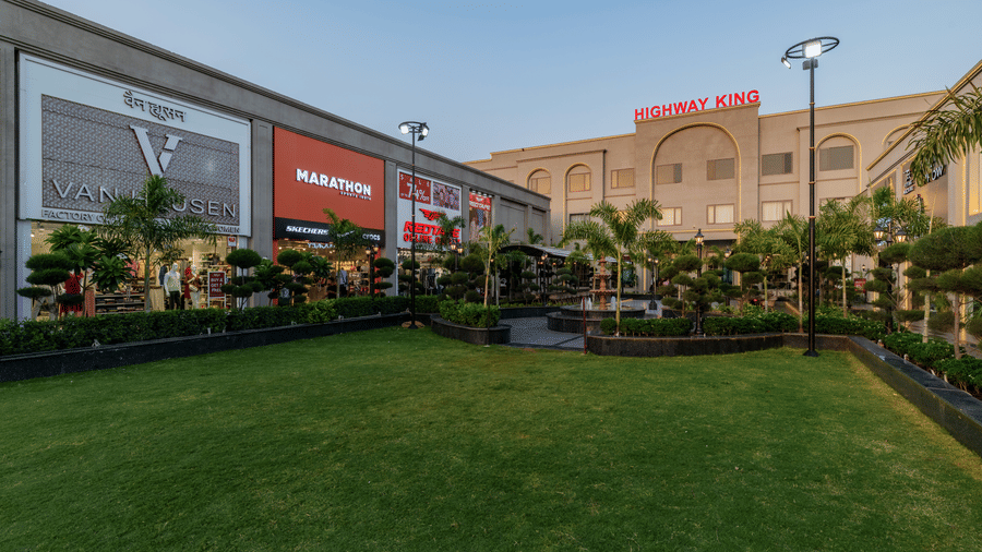 A view of a large lawn, a multi storey building, and retail shops at Hotel Highway King, Harmada.