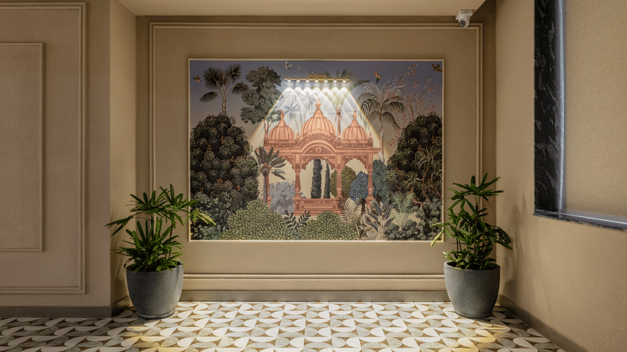 A framed wall painting under a bright spotlight, 2 potted green plants on the floor, and geometric patterned floor tiles at Hotel Highway King, Harmada.