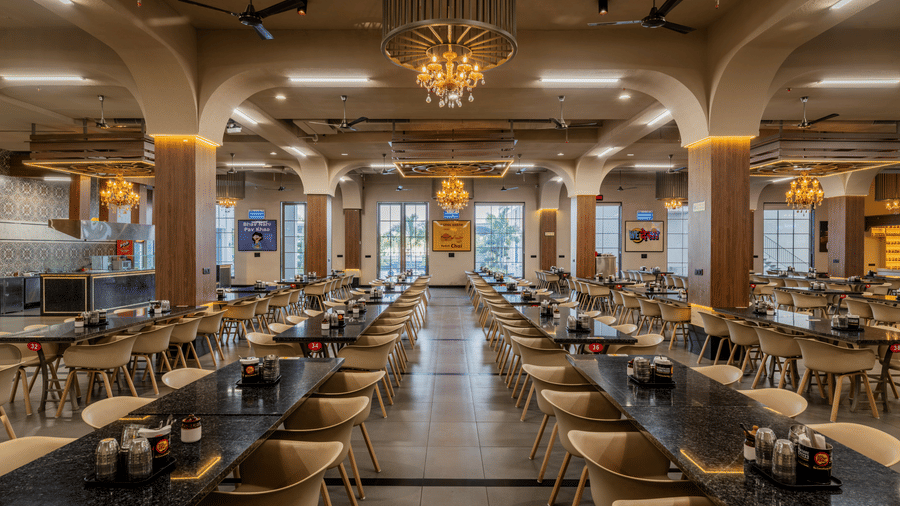 Symmetrical view of a restaurant interior featuring organized tables, matching chairs, and lit chandeliers at Hotel Highway King, Harmada.