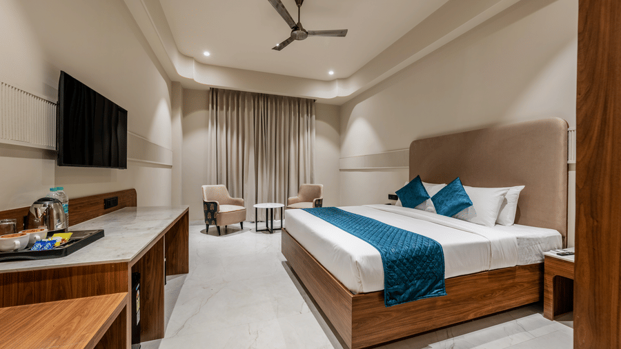 A king size bed, a long wooden desk with a television, and 2 armchairs at Hotel Highway King, Harmada.
