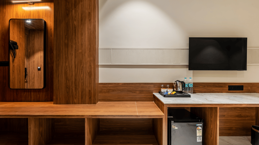 A wooden luggage rack, a mirror, and a desk with a television at Hotel Highway King, Harmada.