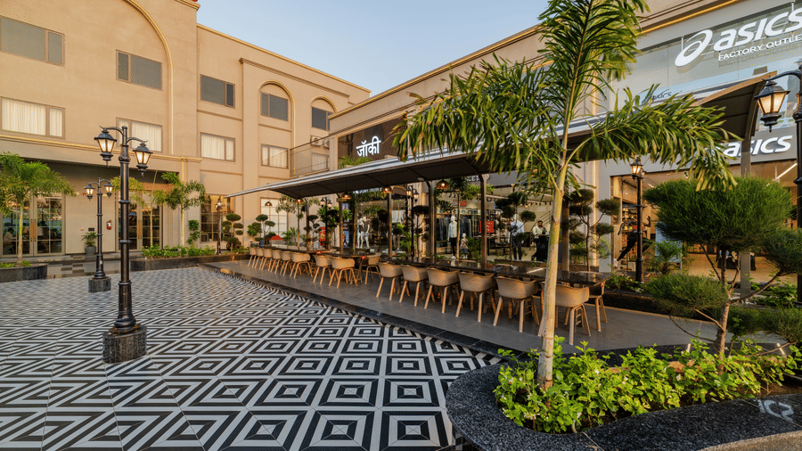 A tiled plaza with outdoor dining setups, lampposts, and store facades at Hotel Highway King, Harmada.