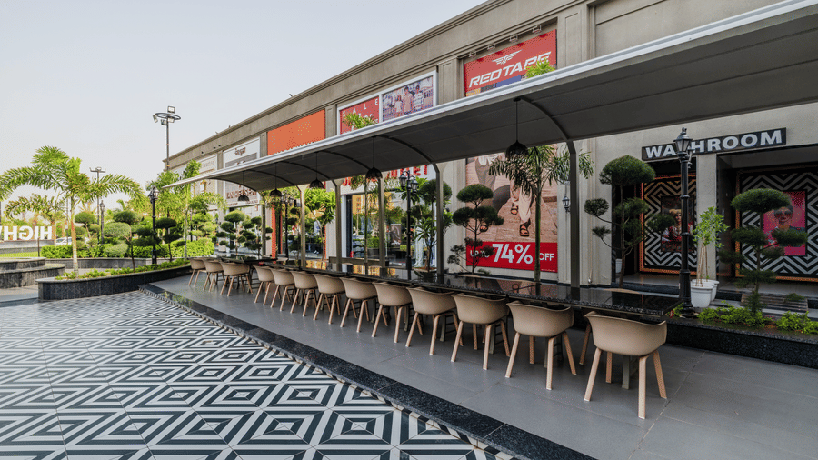 A long row of outdoor dining chairs, storefronts, and a tiled walkway at Hotel Highway King, Harmada.