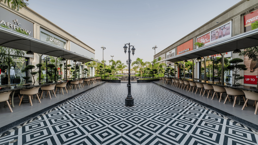 A patterned tiled walkway flanked by dining tables, chairs, and potted plants at Hotel Highway King, Harmada.