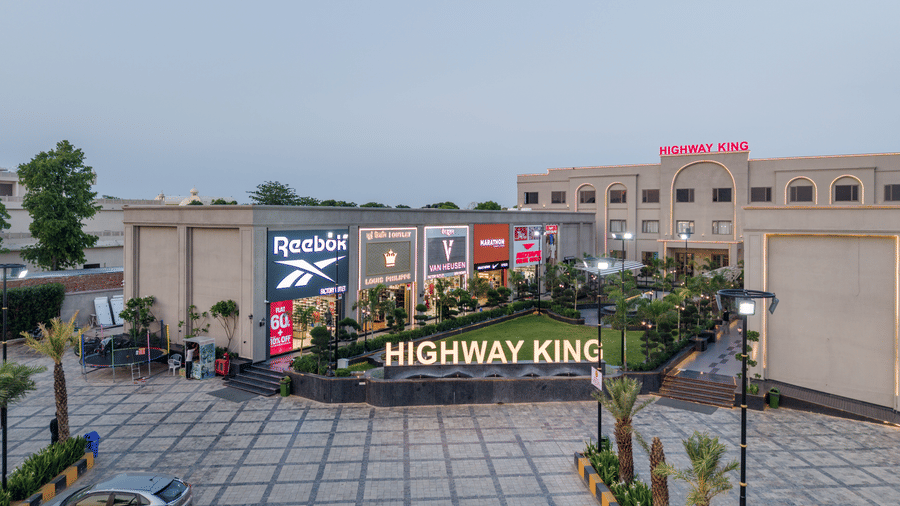 An elevated view of a paved driveway, a landscaped garden courtyard, and a multi storey commercial building exterior at Hotel Highway King, Harmada.