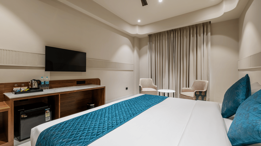 A wall-mounted television, a desk with a mini fridge, and 2 chairs at Hotel Highway King, Harmada.