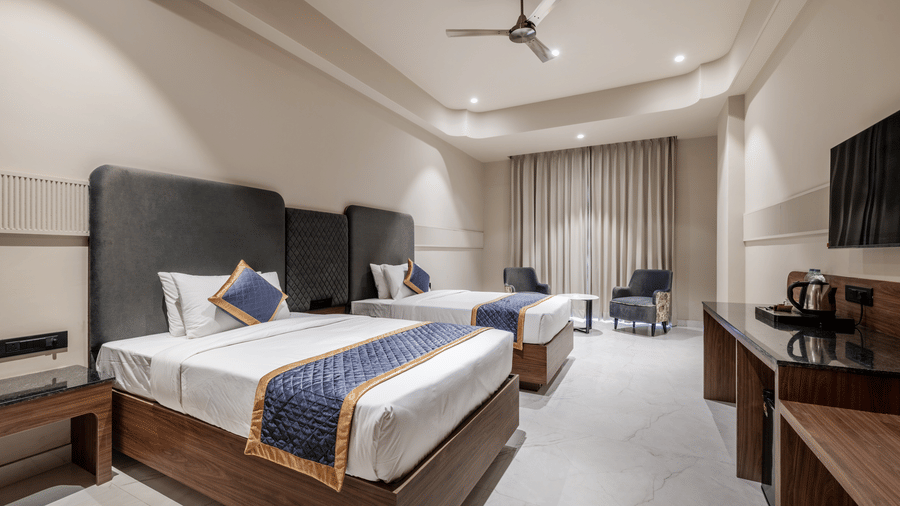 Hotel room setup containing double beds, a flat screen television, and a seating corner with a small table at Hotel Highway King, Harmada.