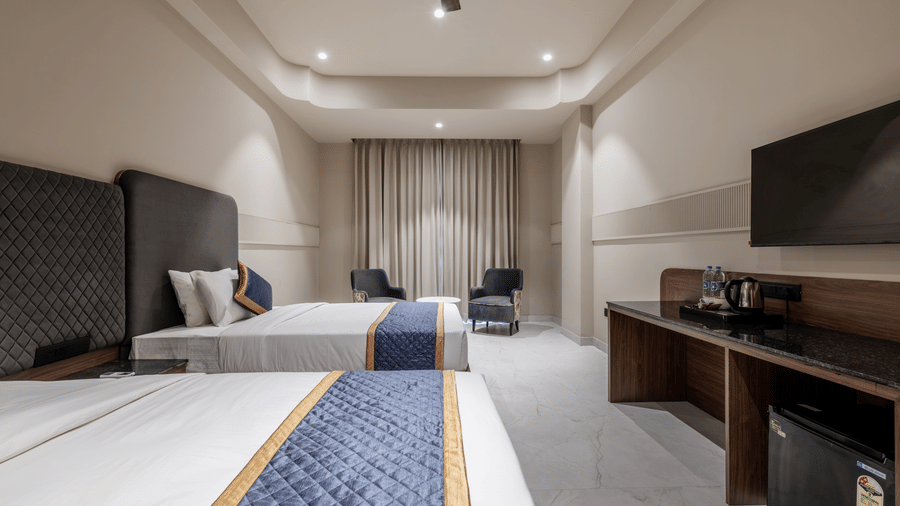 Hotel room featuring 2 separate beds, a wall mounted television, and 2 chairs by the curtained window at Hotel Highway King, Harmada.