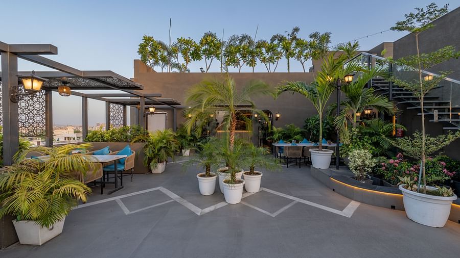 Rooftop dining setup with multiple planters, tables and chairs, and lattice structures at Hotel Highway King, Jaipur.