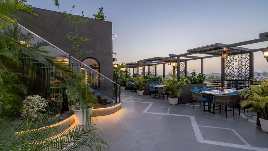 Evening rooftop walkway with potted plants, wall lamps, and covered seating at Hotel Highway King, Jaipur.
