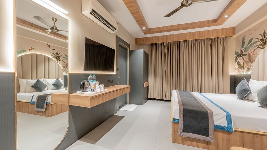 A room with a king size bed, ceiling to floor curtain, wall-mounted TV, wooden desk, and a mirror at Hotel Highway King, Jaipur.