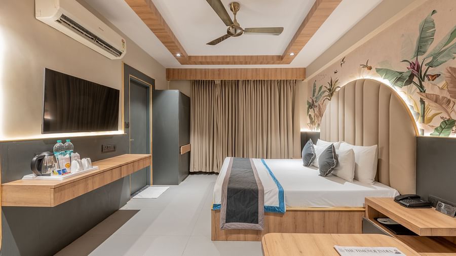 A wide view of the room featuring a king size bed, curtains, TV unit, mirror, and a wall mural at Hotel Highway King, Jaipur.