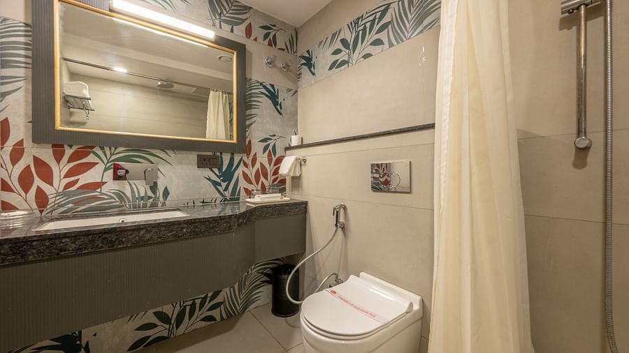 A bathroom with floral wallpaper, washbasin, mirror, and a toilet next to a shower with curtain at Hotel Highway King, Jaipur.