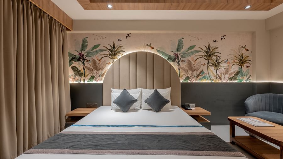 A straight-on view of a king size bed with arched headboard, nightstands and mural on the wall at Hotel Highway King, Jaipur.