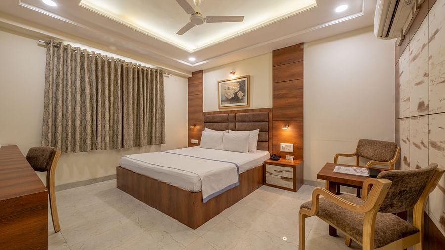 A well furnished spacious room with a king size bed, wooden furniture, and elegant curtains at Hotel Highway King, Jaipur.