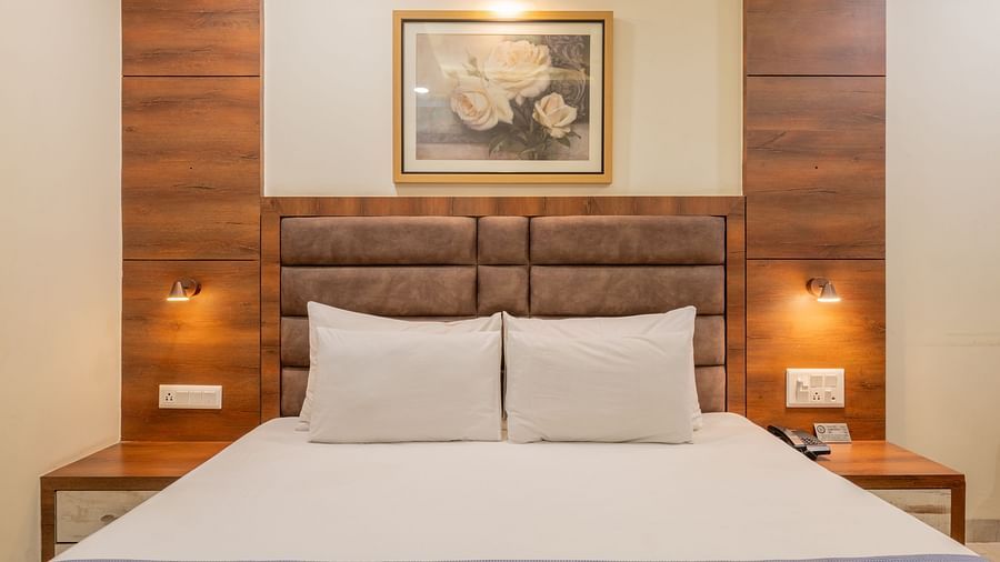 A close-up view of king size bed with padded headboard, two wall lamps, and framed artwork above at Hotel Highway King, Jaipur.