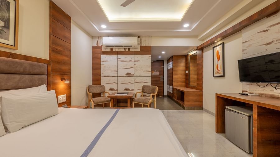 A wide view of a modern room, featuring a king size bed, a TV area, chairs and a table space, and wooden furnishings at Hotel Highway King, Jaipur.